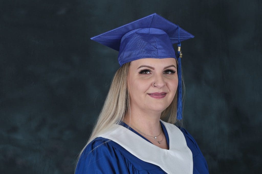 Oksana in her grad cap and gown smiling at the camera.